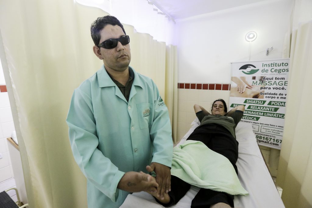 Na foto, homem cego massageia pé de uma mulher deitada na maca.