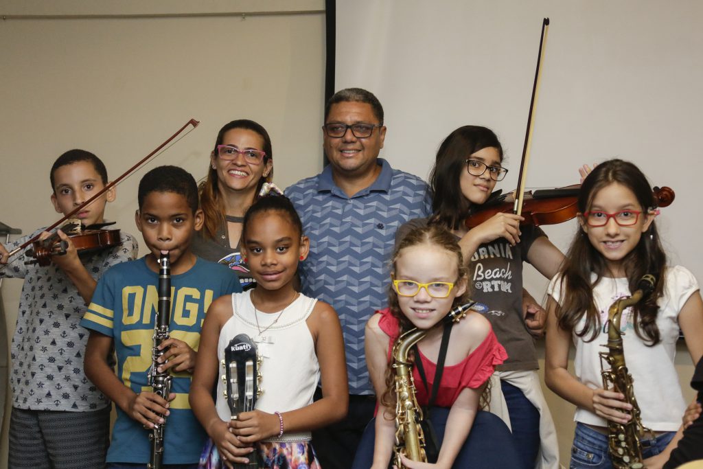 Foto do professor Carlos Alberto com sete alunos do Instituto Sons do Silêncio. Todos sorriem e seguram seus instrumentos musicais.