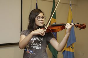 Foto da criança Camilly Lins, que é surda, tocando violino.