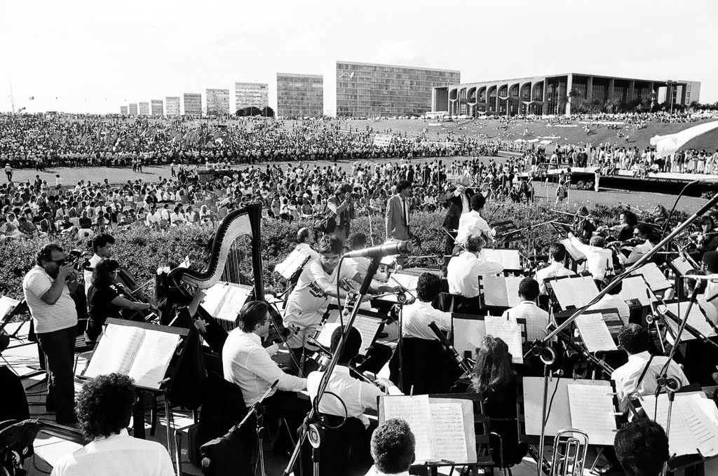 Foto de apresentação da Orquestra Sinfônica (primeiro plano) para milhares de pessoas no gramado do Congresso.