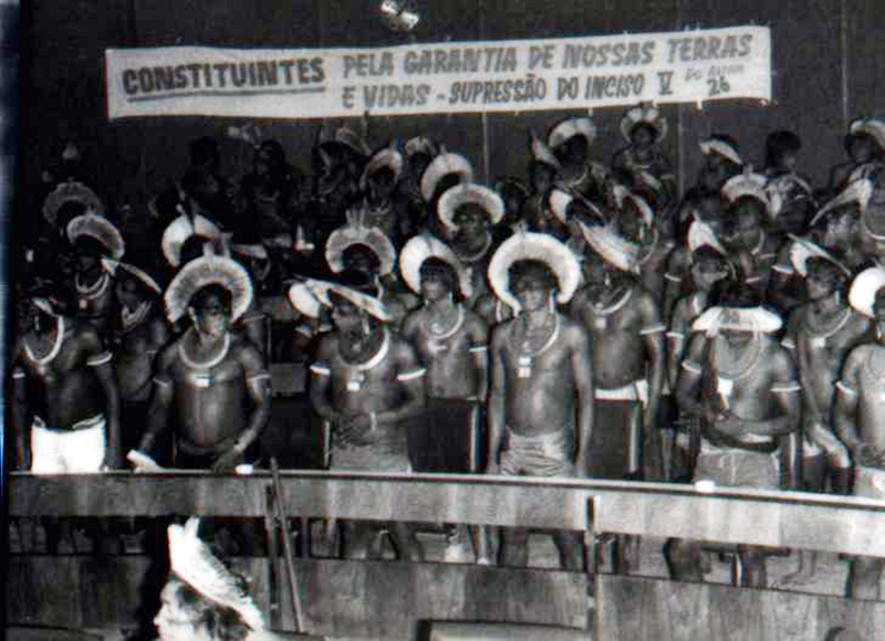 Foto de grupo de índios nas galerias do Congresso Nacional segurando faixa com os dizeres "Constituintes: pela garantia de nossas terras e vidas, supressão do inciso cinco".