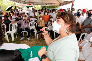 Deputada, usando máscara, fala para plateia em bancos de plástico no sítio Roncadorzinho