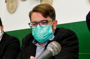 Em mesa em lugar fechado, o secretário usa óculos e máscara cirúrgica