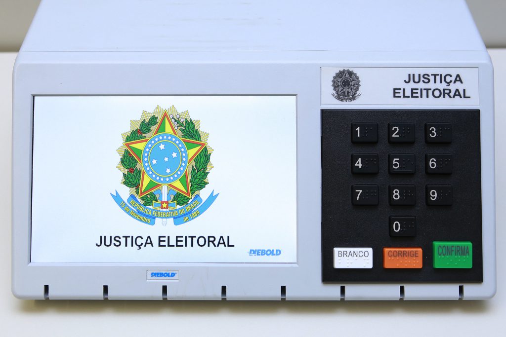 Foto da urna eletrônica, com logotipo da Justiça Eleitoral na tela