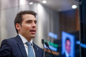 Deputado fala ao microfone do Plenário, usando terno azul marinho e gravata azul clara.