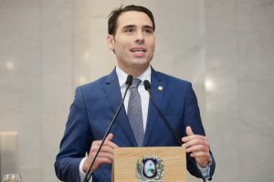 Foto do Deputado João Paulo Costa falando na tribuna, usando terno azul marinho e gravata cinza