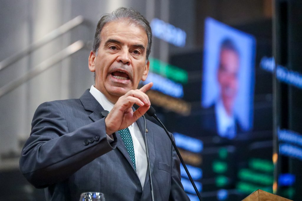 Deputado Alberto Feitosa, usando terno risca de giz, fala na Tribuna, com o painel do Plenário desfocado ao fundo