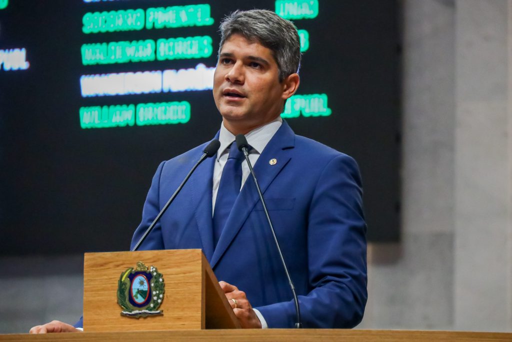 Deputado Renato Antunes, com terno azul escuro e gravata da mesma cor, fala na tribuna, com painel aparecendo ao fundo