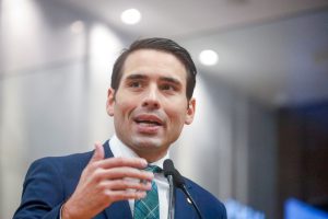 Deputado João Paulo Costa fala na tribuna, utilizando terno azul escuro e gravata com tons de verde