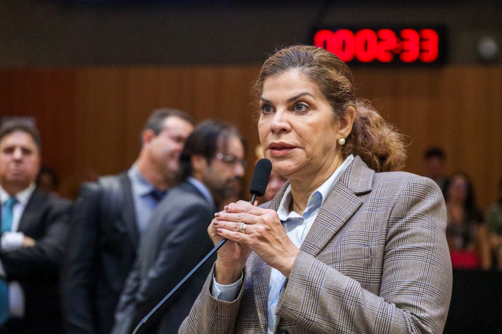 Deputada Socorro Pimentel fala no microfone do Plenário, enquanto aparece relógio cronometrando o tempo ao fundo, junto com outros deputados reunidos, em imagem desfocada
