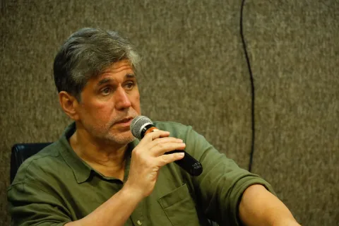 Homem branco, de cabelo grisalho, usando camisa social verde musco, fala ao microfone.
