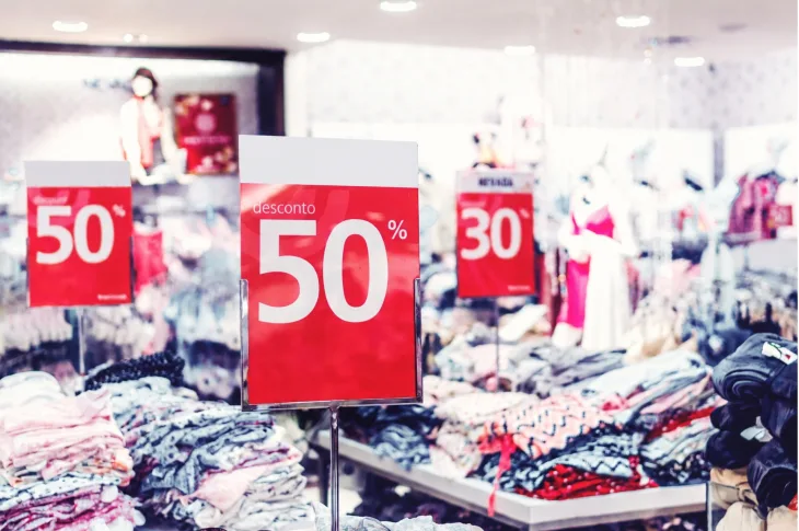 Foto de uma loja de departamentos com roupas em oferta, com placas vermelhas com descontos de 50 e 30%