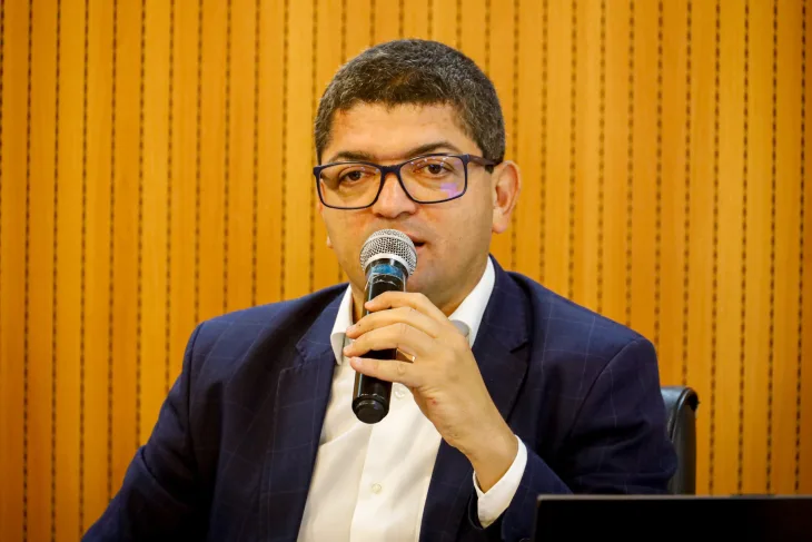 Homem pardo de óculos, usando blazer azul marinho com camisa branca