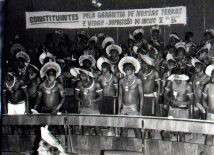 Foto de grupo de índios nas galerias do Congresso Nacional segurando faixa com os dizeres "Constituintes: pela garantia de nossas terras e vidas, supressão do inciso cinco".